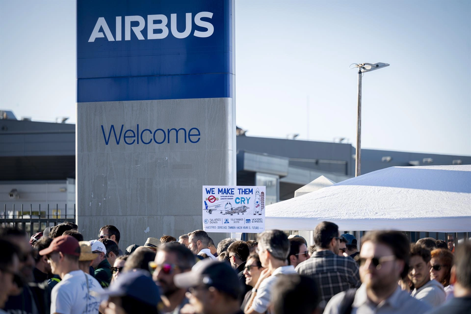Fotografía editorial que muestra a trabajadores de Airbus concentrados frente a un cartel de bienvenida corporativo de la empresa durante una protesta laboral.