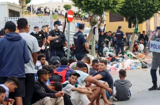 Policías nacionales españoles controlando a migrantes sentados en el suelo durante una crisis migratoria fronteriza.