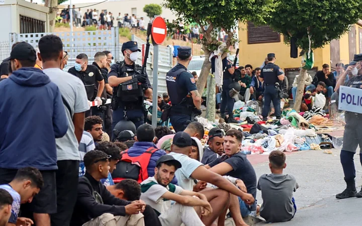 Policías nacionales españoles controlando a migrantes sentados en el suelo durante una crisis migratoria fronteriza.