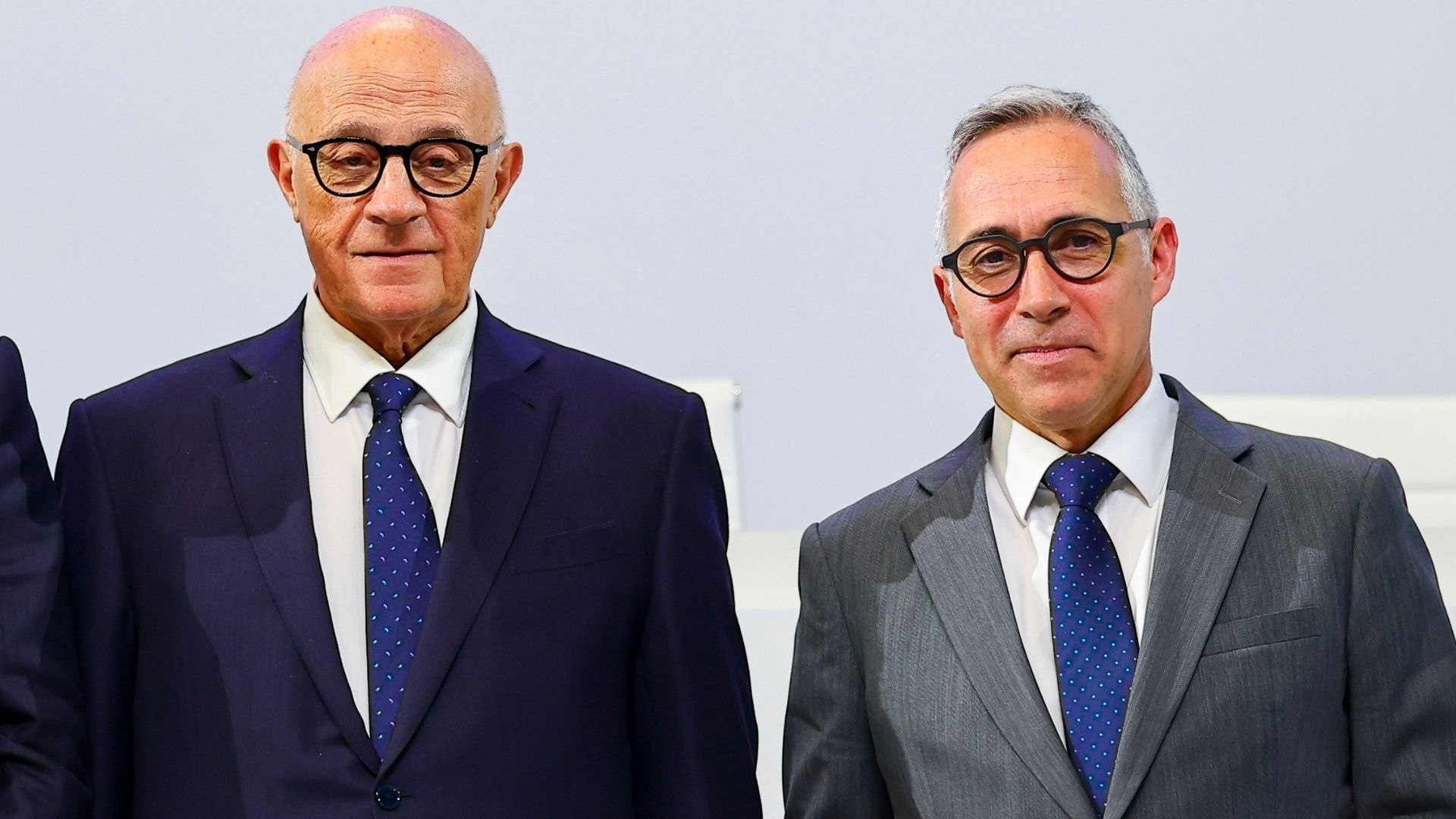 Fotografía editorial de dos ejecutivos bancarios trajeados con corbata y gafas mirando a cámara.