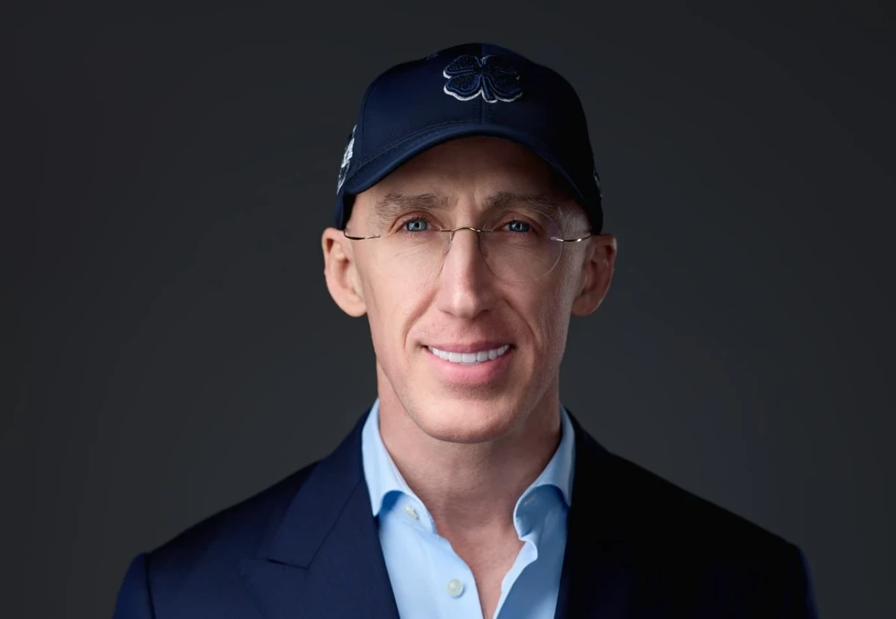 Retrato de Uri Poliavich con gorra azul, gafas y americana oscura sobre fondo neutro.
