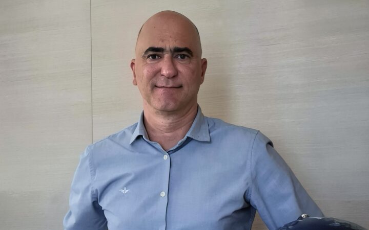 Retrato de un hombre calvo con camisa azul en una oficina con panel de madera de fondo.