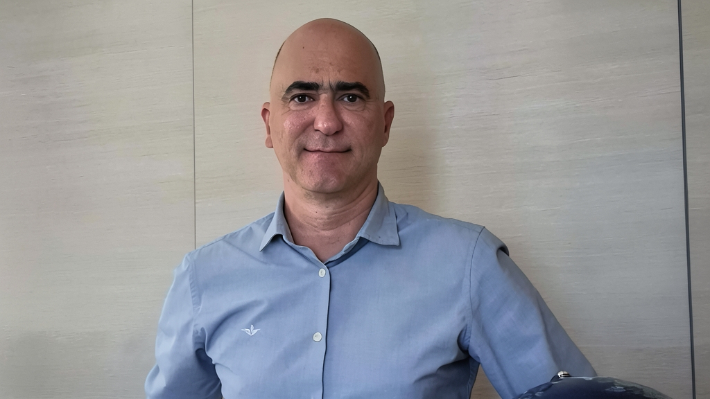 Retrato de un hombre calvo con camisa azul en una oficina con panel de madera de fondo.