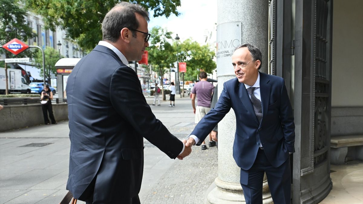 Dos hombres en traje estrechándose la mano en una calle de Madrid frente a la sede de la CNMC.
