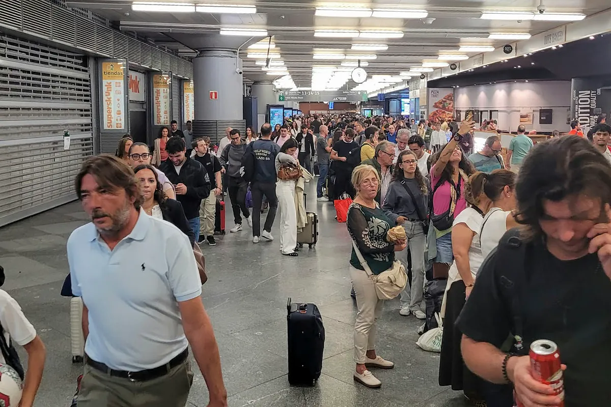 Multitud de pasajeros esperando en una concurrida estación de tren con maletas y paneles informativos tras las incidencias en la línea de alta velocidad.