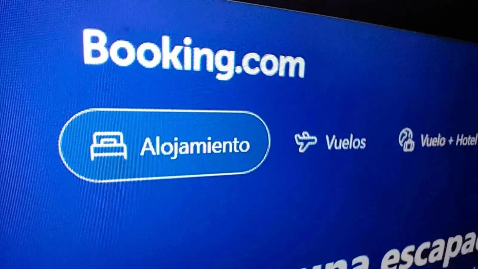 Fotografía de una pantalla mostrando el logotipo y la interfaz de la plataforma de reservas Booking.com con los botones de Alojamiento y Vuelos.