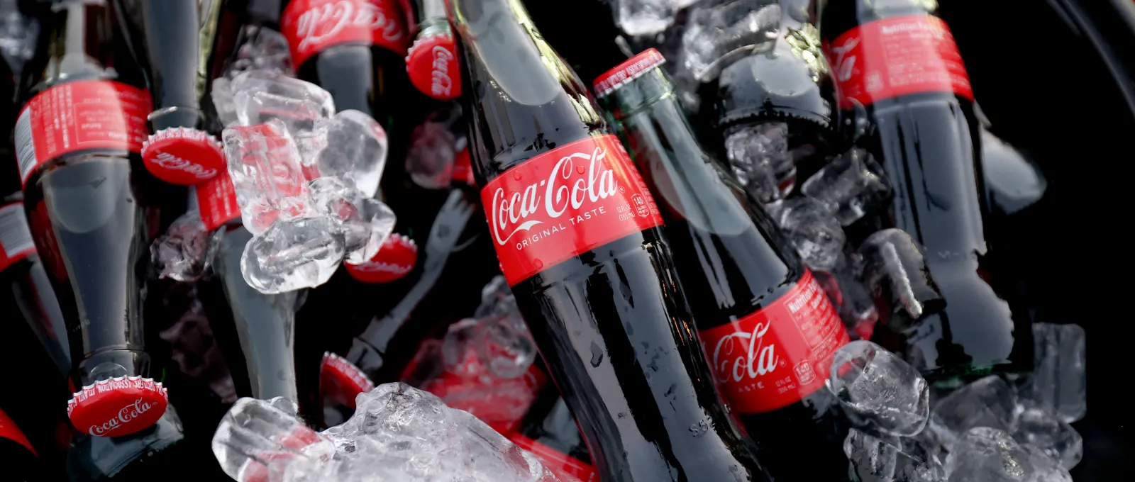 Varias botellas de Coca-Cola enfriándose en un cubo lleno de cubitos de hielo.