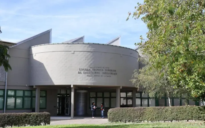 Fachada exterior de la Escuela Técnica Superior de Ingeniería Industrial de la Universidad de Vigo, con un edificio de estructura semicircular y ventanales verdes.