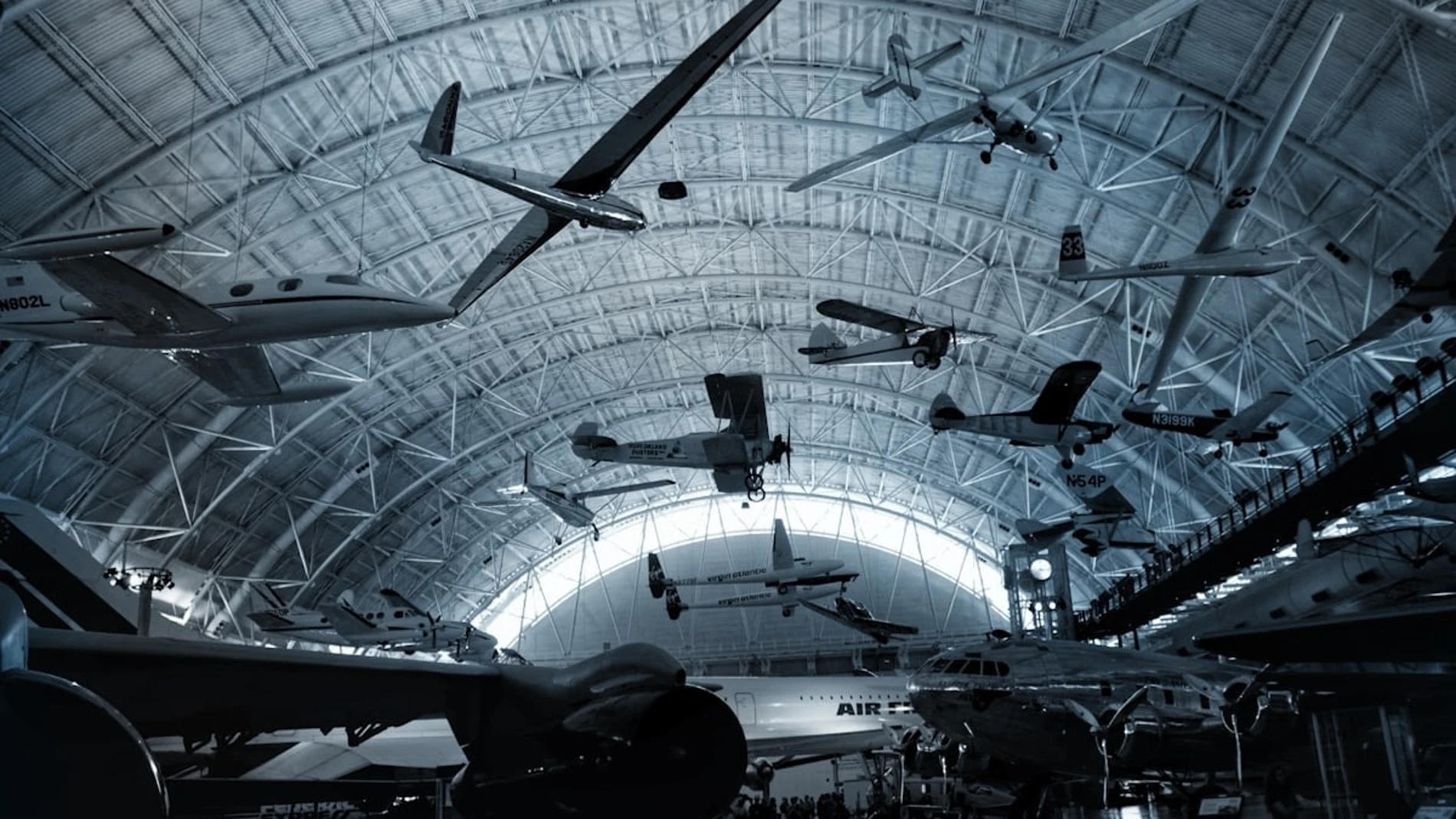 Fotografía de un museo aeronáutico con múltiples aviones históricos y planeadores colgados del techo en una gran estructura metálica abovedada.