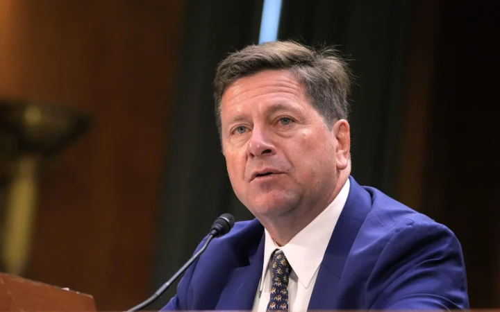 Fotografía editorial de Jay Clayton hablando en una audiencia pública ante un micrófono.