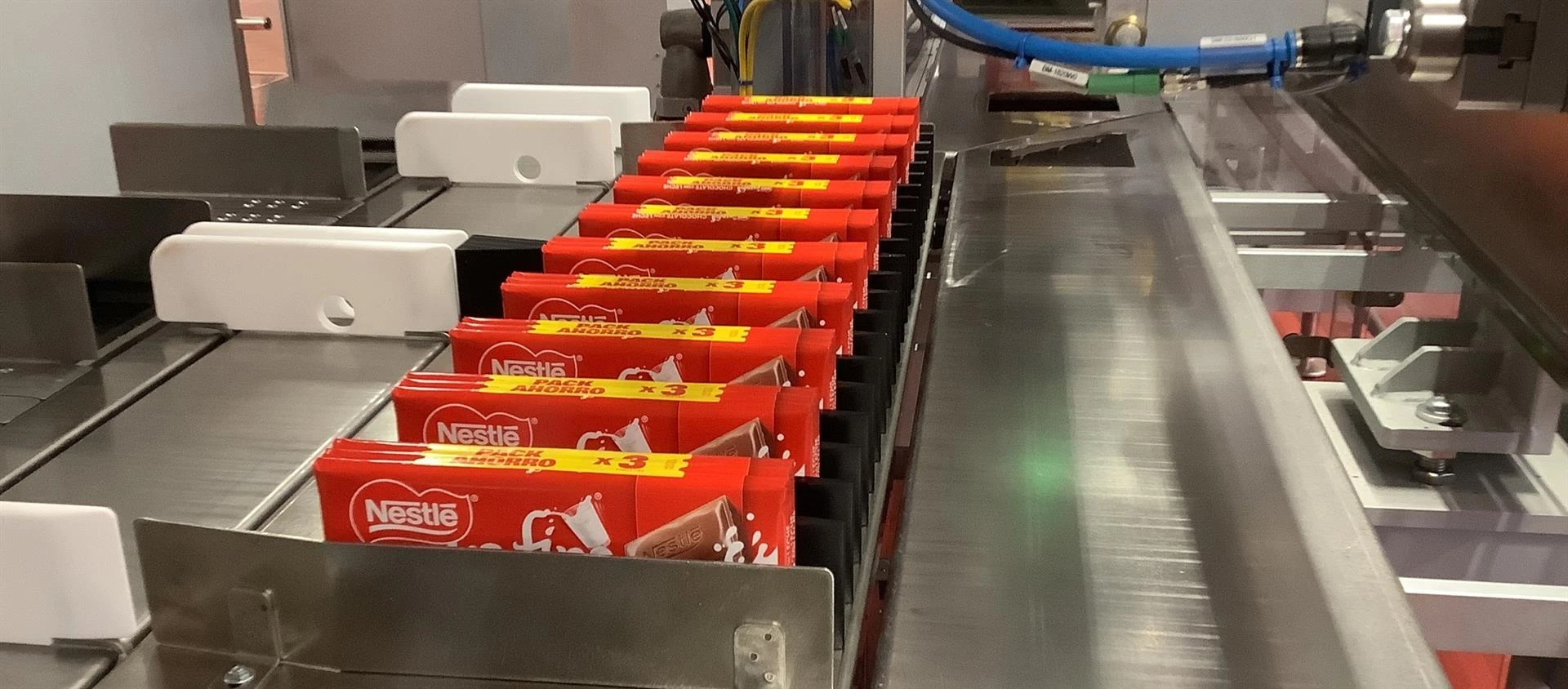 Línea de producción automatizada en una fábrica de Nestlé con barras de chocolate empaquetadas en una cinta transportadora.